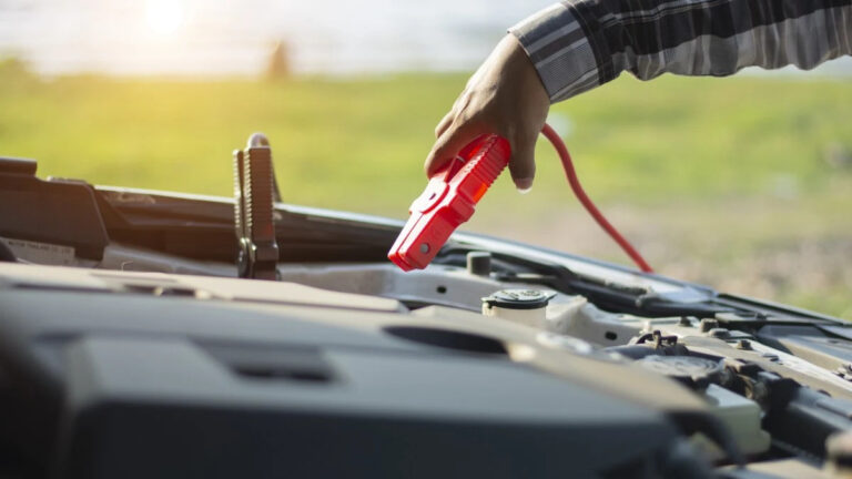 close up of mechanic attaching jumper cables to car battery