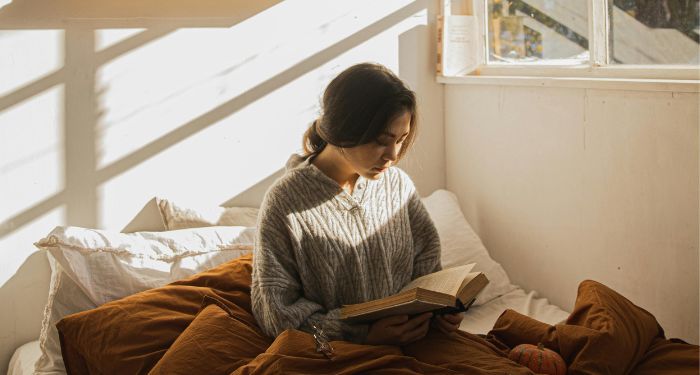 fair skinned woman reading in bed with fall decorations around her.jpg.optimal