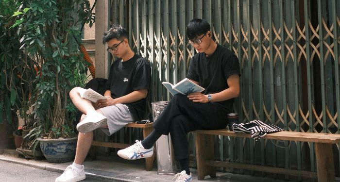 two lAsian men reading outside on a bench.jpg.optimal