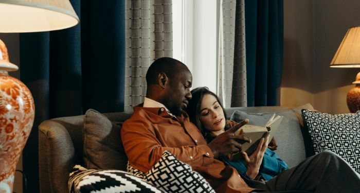 a dark brown skinned Black man and a fair skinned white woman reading a book on a couch.jpg.optimal