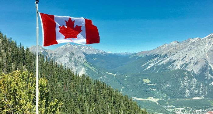 canadian flag flying against backdrop of forested mountains.jpg.optimal