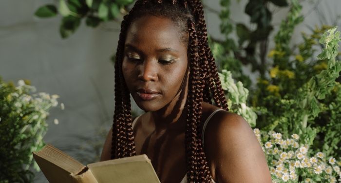 dark skinned Black woman with brown braids reading a book with plants in the background.jpg.optimal
