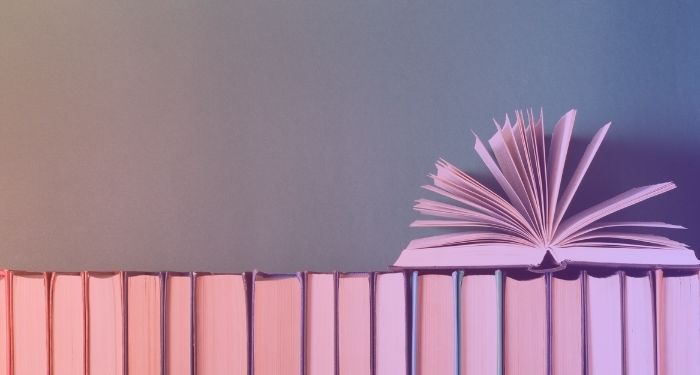 open book on top of books in a row with spines faced away and pink gradient overlay.jpg.optimal